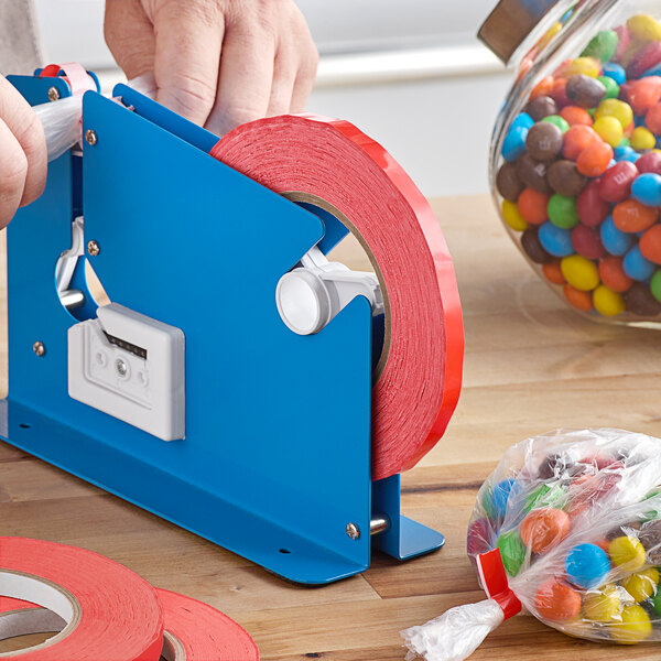 A hand using a blue tape dispenser to seal a plastic bag with red Lavex tape.