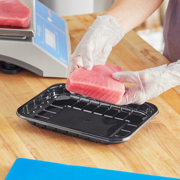 A person in gloves weighing a piece of meat on a black PET plastic meat tray.