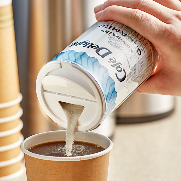 A hand pouring Cafe Delight non-dairy creamer into a cup of coffee.