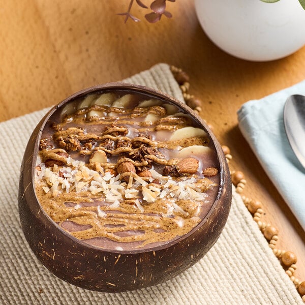 A bowl of smoothie with nuts and almond butter on a table.