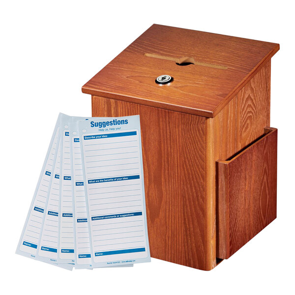 An AdirOffice oak wood wall mounted suggestion box with suggestion cards on a table next to a few papers.