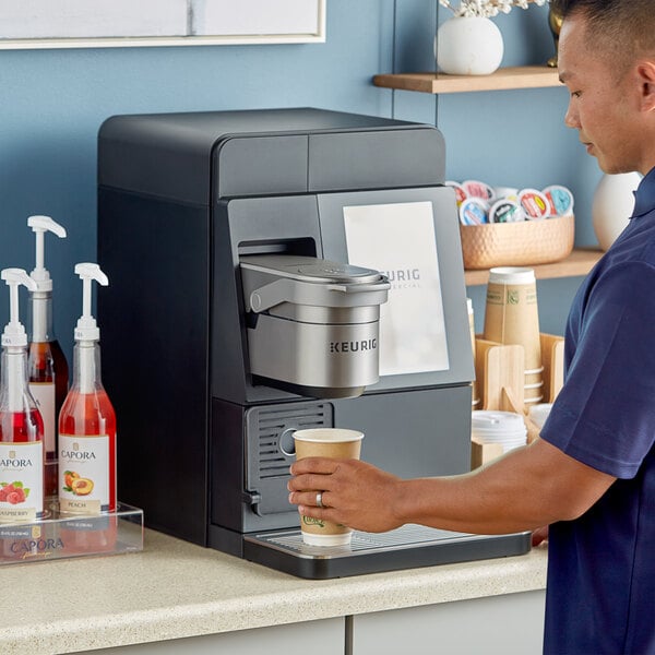 A man pouring coffee into a cup from a Keurig single serve coffee machine.