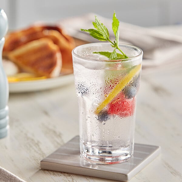 A highball glass of water with berries and a leaf on top.