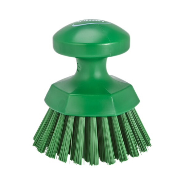 A close-up of a green circular Vikan scrub brush with stiff bristles.