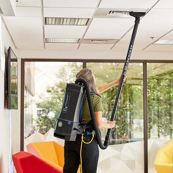 A woman using a Lavex backpack vacuum cleaner in a corporate office cafeteria.