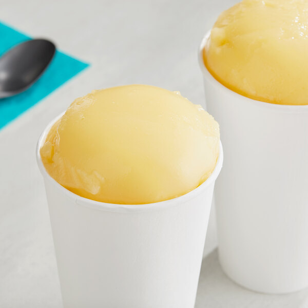 Two cups of Philadelphia Water Ice Peach Italian Ice with yellow spoons.