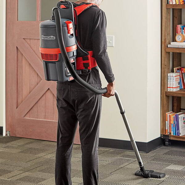 A man wearing a NaceCare Solutions cordless backpack vacuum cleaning a floor.