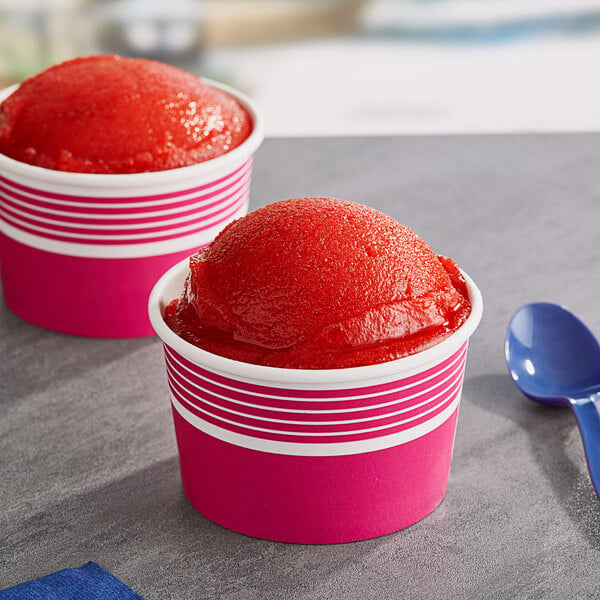 Two cups of Philadelphia Water Ice Strawberry Italian Ice on a table with a blue spoon.
