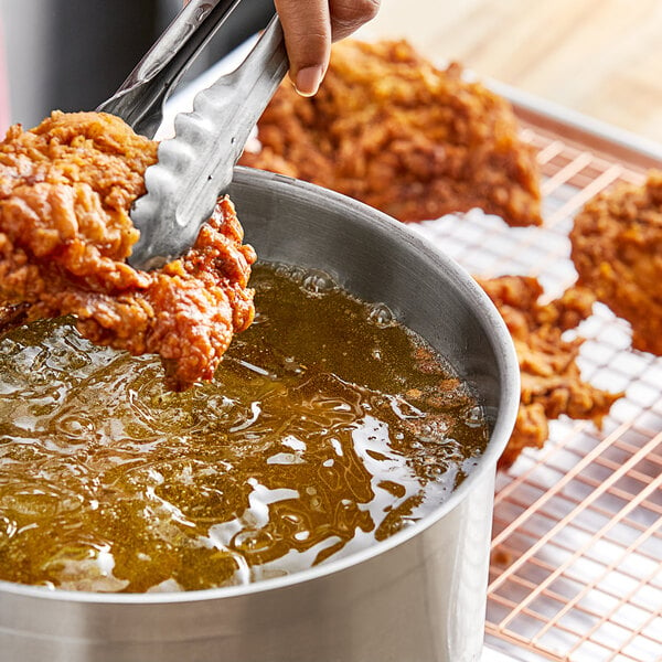 A person using tongs to fry a Stratas Primex Golden Flex Donut Fry Shortening coated chicken in a pot of liquid.