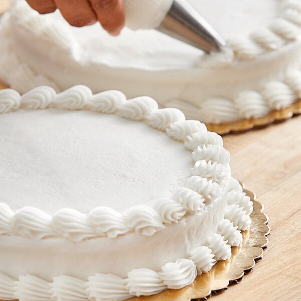 A person using Stratas Sweetex Golden Flex Icing Shortening to decorate a cake with a pastry bag.
