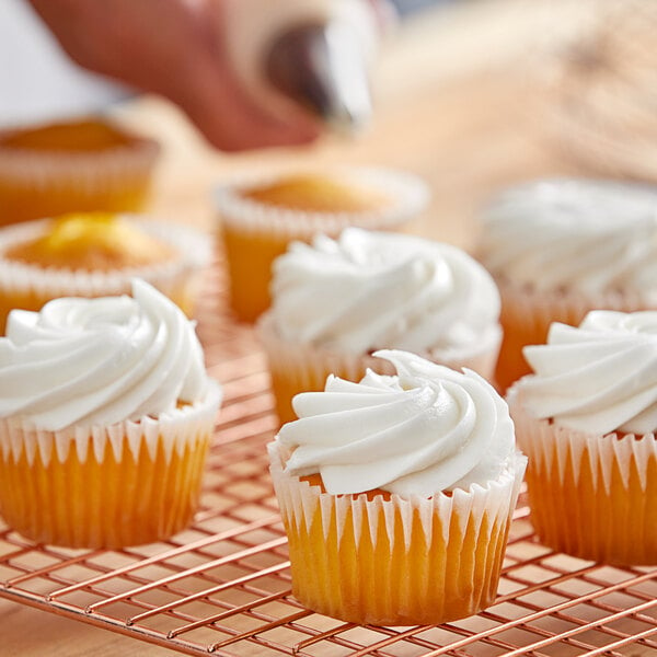 A cupcake with white frosting on a cooling rack.