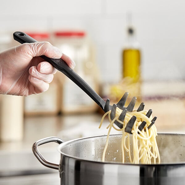 A person using a black Choice heat-resistant nylon pasta fork to stir noodles in a pot.