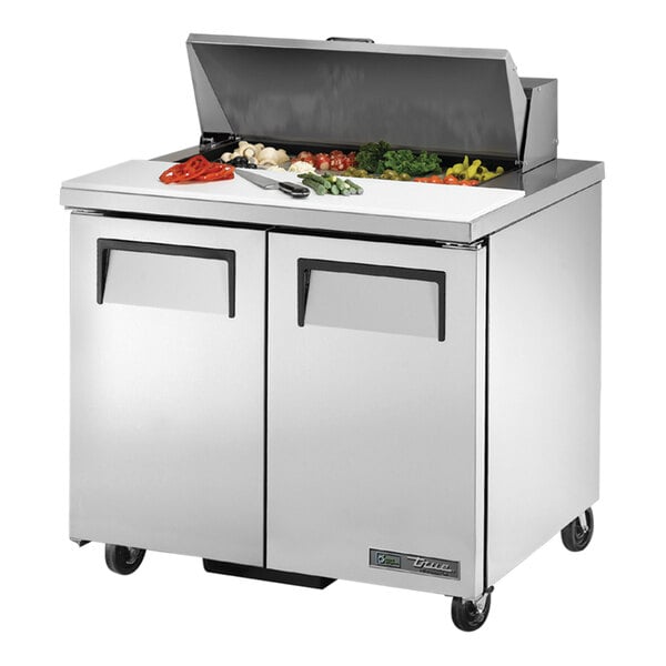 A True 2 door refrigerated sandwich prep table on a counter with food on top.
