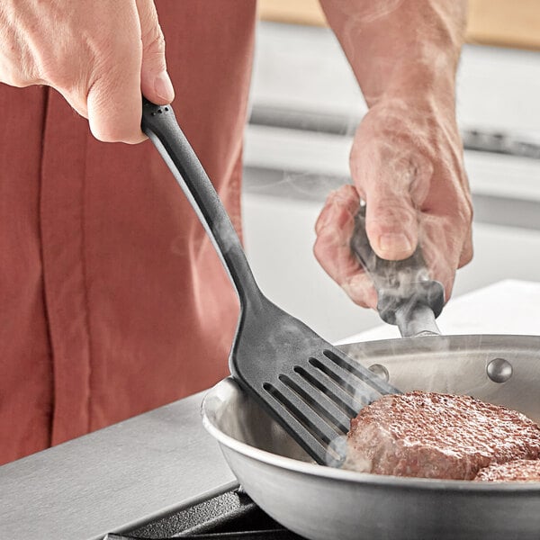 A person using a Choice black slotted turner to cook meat in a pan.