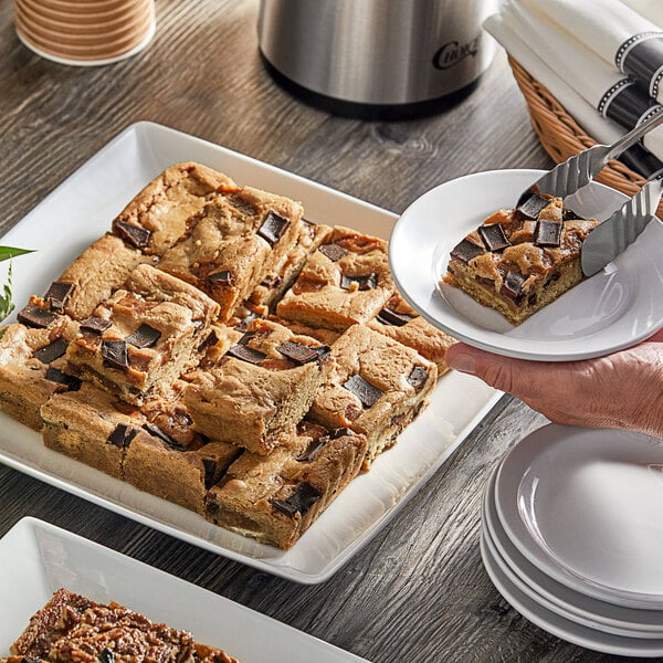 A hand holding a plate of Sweet Street Desserts Toffee Crunch Blondie bars.