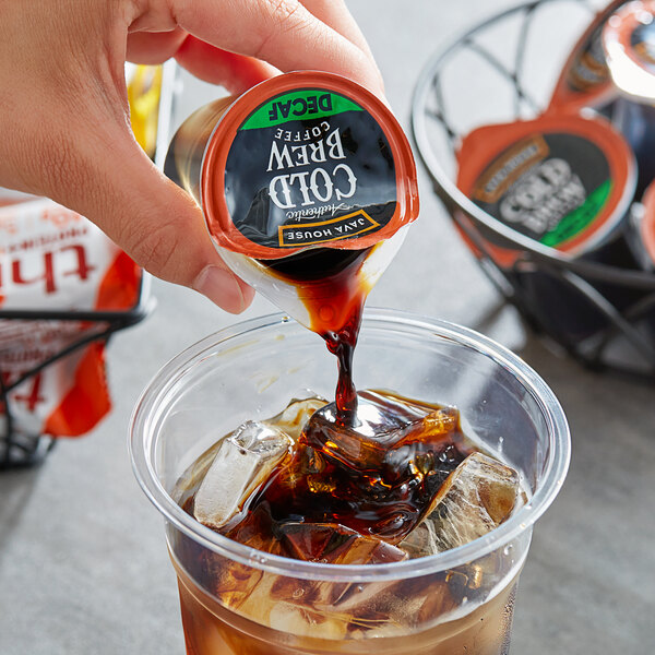 A hand pouring Java House decaf cold brew coffee into a cup of ice.