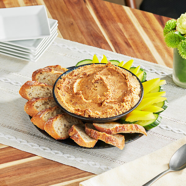 A plate of Rind Tomato 'Nduja Plant-Based Cream Cheese spread with bread and vegetables.