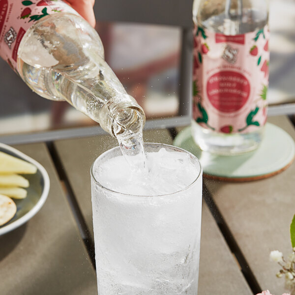 A person pouring Reading Soda Works Strawberry Mint Lemongrass soda into a glass of ice.
