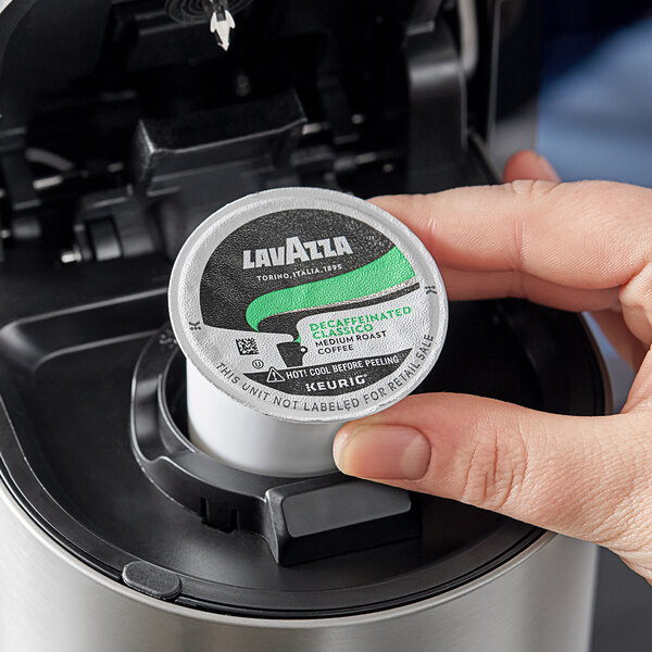 A hand holding a small round container of Lavazza Decaf Classico Coffee Single Serve K-Cup Pods.