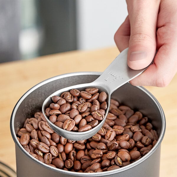 A person using a Planetary Design stainless steel coffee scoop to measure coffee beans.