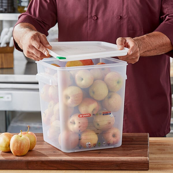 A man holding a Araven translucent plastic container full of apples with a lid