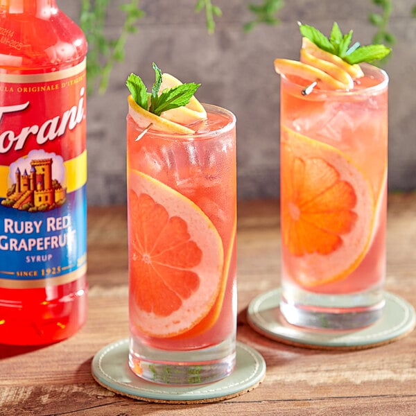 A glass of Torani Ruby Red Grapefruit flavored drink with slices of grapefruit on it.