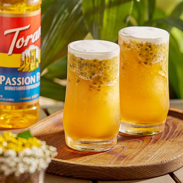 Two glasses of Torani passion fruit flavoring syrup on a wooden tray.