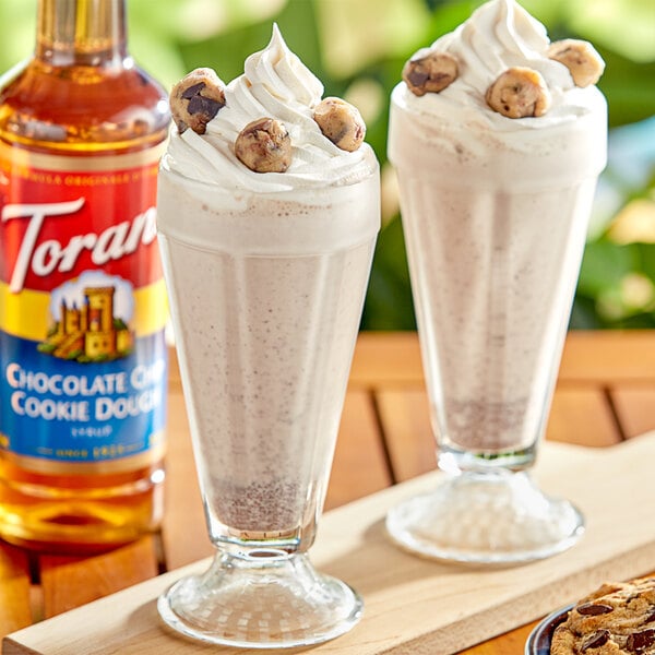 A glass of chocolate milk with a straw and a cookie next to a bottle of Torani Chocolate Chip Cookie Dough flavoring syrup.