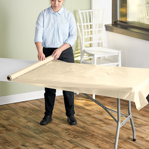 A woman rolling a table with a roll of plastic table cover.