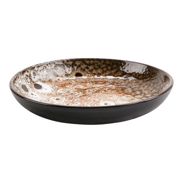 A terracotta bowl with brown and white spots filled with liquid on a table.
