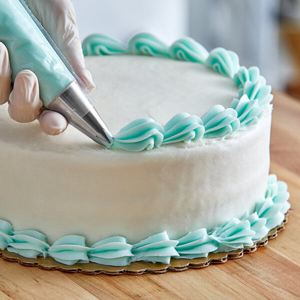 A hand using a Wilton 1M piping tip to decorate a cake with a pastry bag.