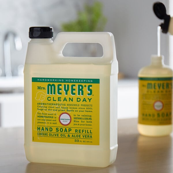 A white plastic jug of Mrs. Meyer's Clean Day Honeysuckle Scented Hand Soap with a yellow label on a counter.