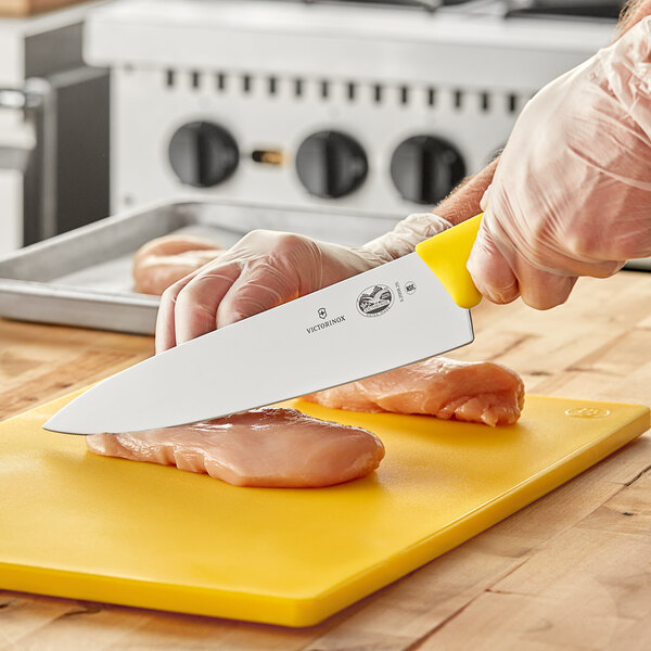A person using a Victorinox chef knife to cut meat on a yellow cutting board.
