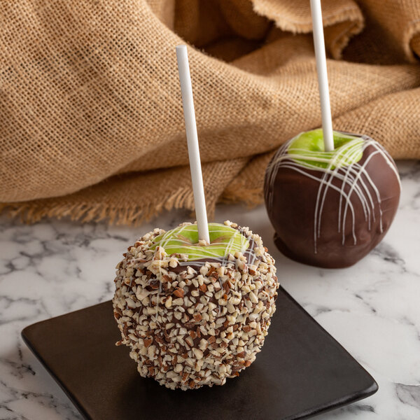 A chocolate covered apple with nuts on a Paper Pointed Candy Apple Stick on a plate.