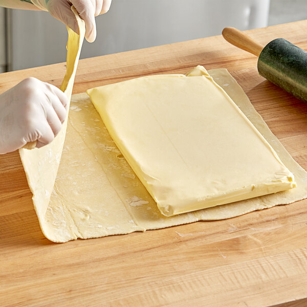 A person using a White Toque unsalted butter sheet to make pastry dough on a wooden surface.