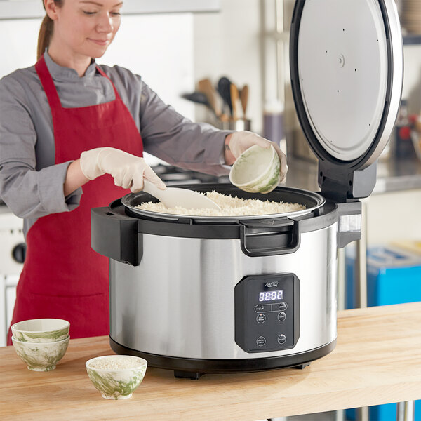 A woman using an Avantco non-stick pot to cook rice in a rice cooker.