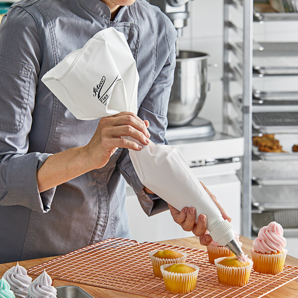 A person holding a Ateco pastry bag full of frosting and decorating a cupcake.