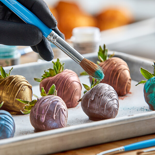 A hand using an Ateco pastry brush to paint chocolate on a strawberry.