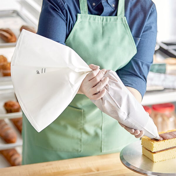 A person wearing a green apron using an Ateco pastry bag to decorate a cake.