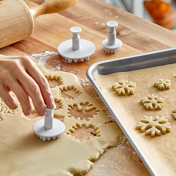 A person's hand using an Ateco snowflake cookie cutter to cut out snowflakes from dough.