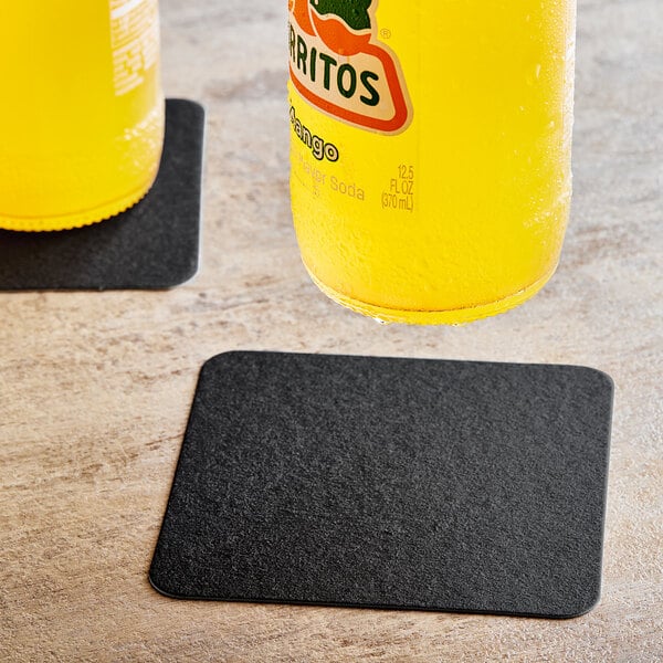 A bottle of orange juice on a table with a Hoffmaster black pulpboard coaster.
