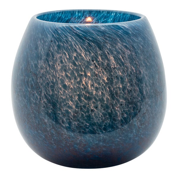A blue Hollowick Marine Art Glass votive with a lit candle in it.