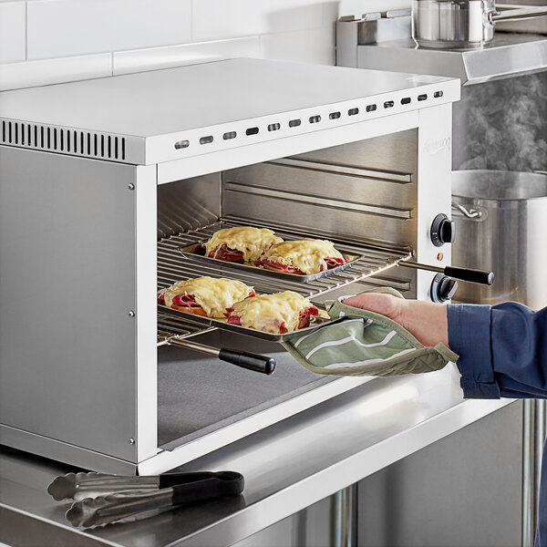 A person using a glove to put food in an Avantco countertop cheese melter.