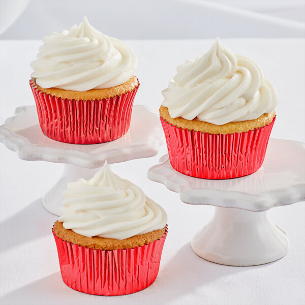 Three Enjay red foil cupcakes with white frosting on white pedestals.