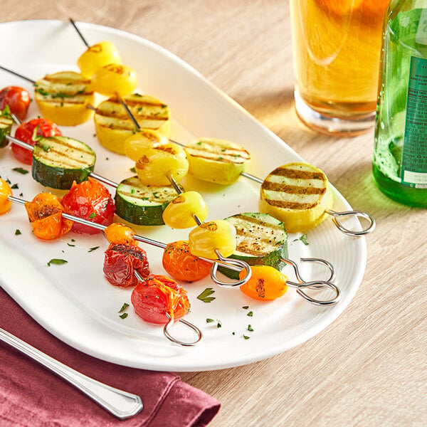 A plate of Choice stainless steel round skewers with grilled zucchini, vegetables, and a glass of beer on a table.