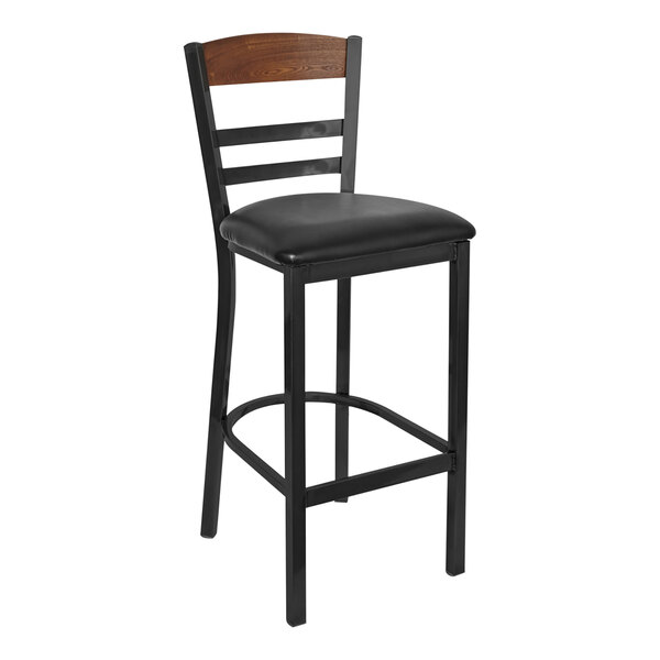 A BFM Seating black metal barstool with black vinyl seat and wooden back.