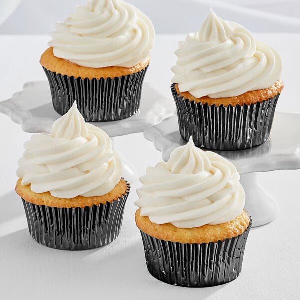 Three Enjay black foil baking cups with cupcakes with white frosting.