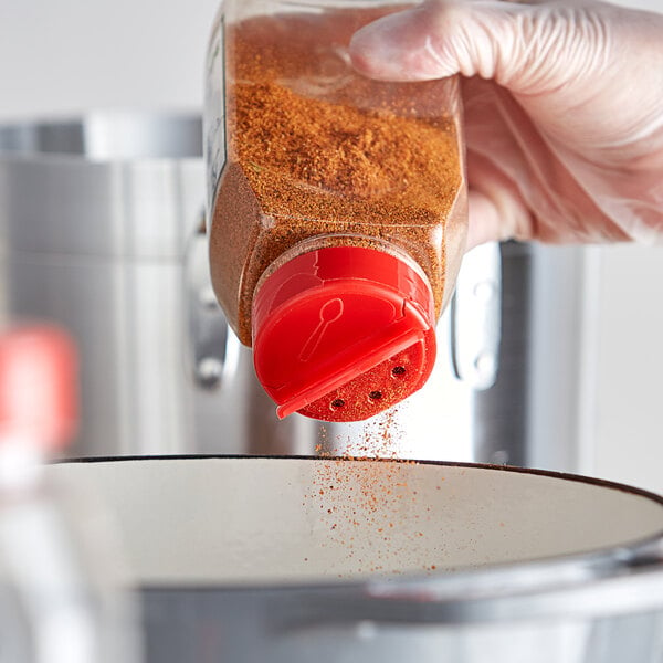 A hand using a 53/485 red dual-flapper spice lid to pour seasoning into a bowl.