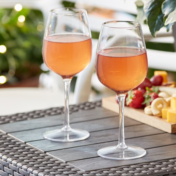 Two Acopa Endure Tritan plastic wine glasses on a table with a glass of wine and fruit.
