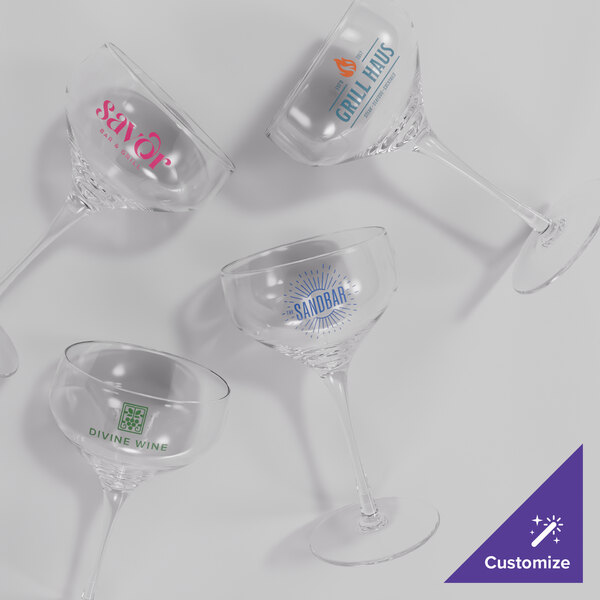 A set of four clear plastic coupe glasses, each with a different custom logo printed on the bowl.